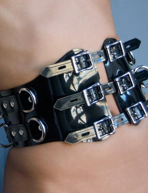 A close-up of a woman's waist in the Black PVC Waist Cincher is shown. The cincher has three adjustable straps in the center, each with two lockable buckles. There are four metal D-rings on each side.