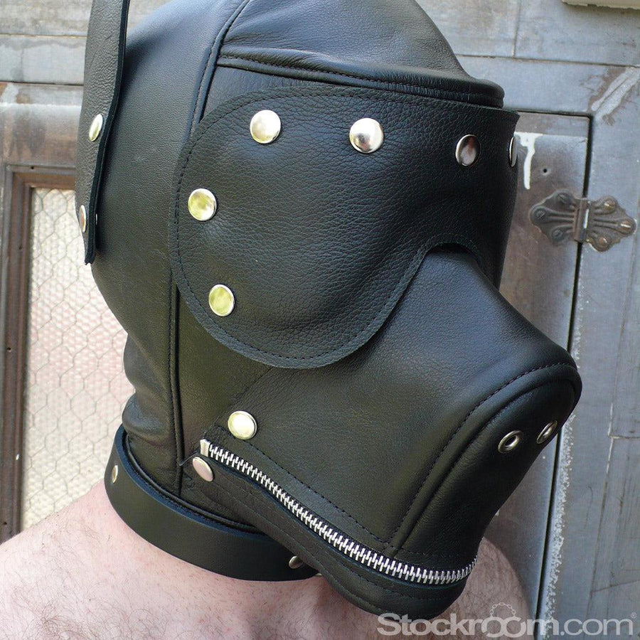 A close-up of a man wearing the Leather Dog Hood with Snap-on Muzzle, Blindfold and Gag and standing outdoors is shown. The hood covers his entire face. The muzzle is zipped closed and the blindfold is on. There are small holes in the muzzle for air.