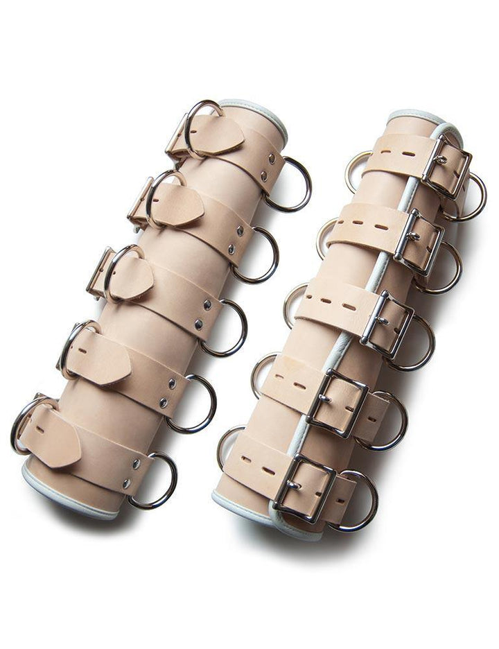 The BDSM Deluxe Medical Leather Arm Splints are shown against a blank background. They are long tubes of tan leather with white accents. The splints have five adjustable straps with lockable metal buckles. Each strap has two D-rings on either side. 