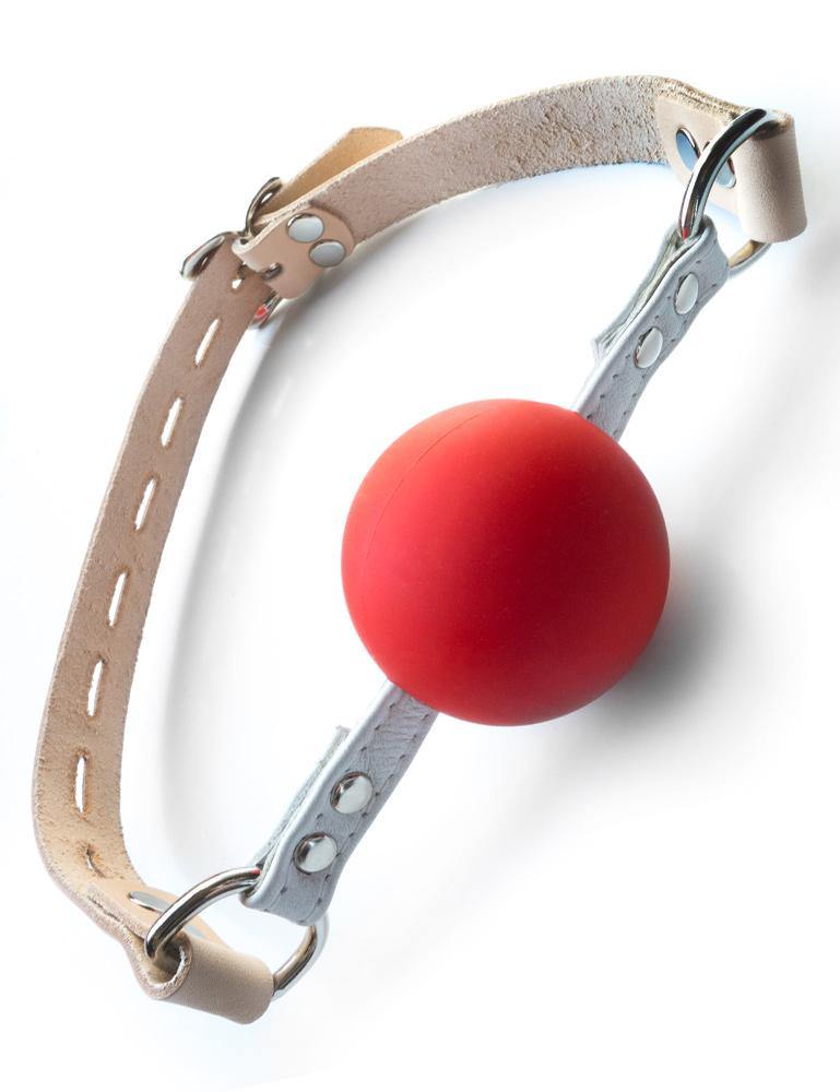 The Medical Silicone Ball Gag is shown against a blank background. The gag is made of a matte red silicone ball with white leather strips on each side. These strips are connected via silver D-rings to an adjustable tan leather strap.