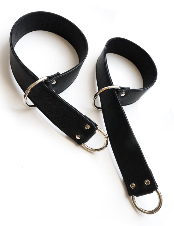 A pair of Garment Leather General Purpose Bondage Straps are shown against a blank background. They are wide strips of black leather with a metal D-ring on each end. One end of the strap has been pulled through the opposite D-ring to create a loop.