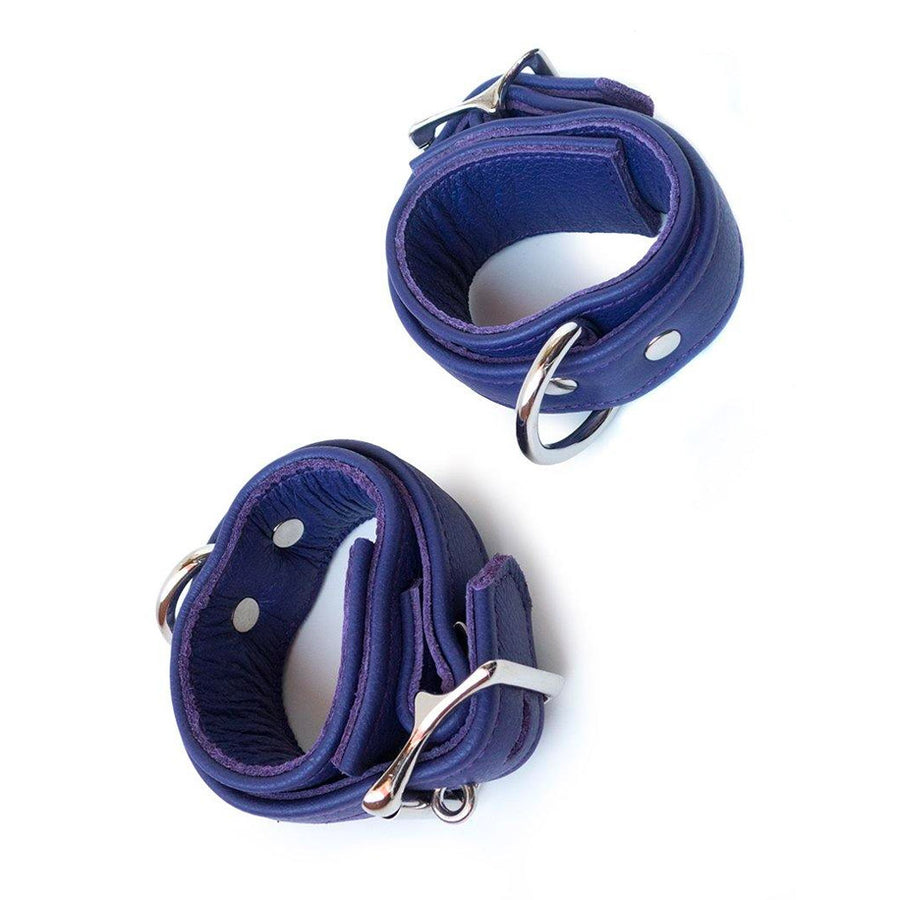 A pair of Premium Garment Leather BDSM Wrist Cuffs are shown against a blank background. They are made of purple leather and silver hardware. Each cuff has an adjustable strap, a lockable buckle closure, and a D-ring.