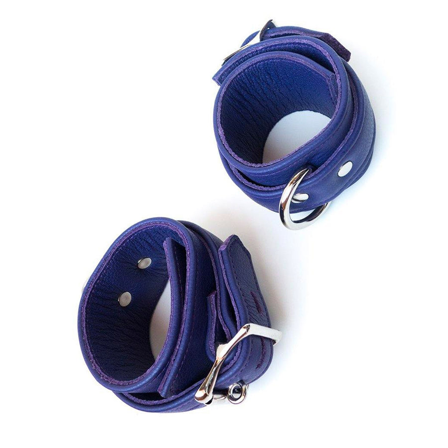 A pair of Premium Garment Leather BDSM Ankle Cuffs are shown against a blank background. They are made of purple leather and silver hardware. The cuffs have an adjustable strap, a lockable metal buckle, and a D-ring.