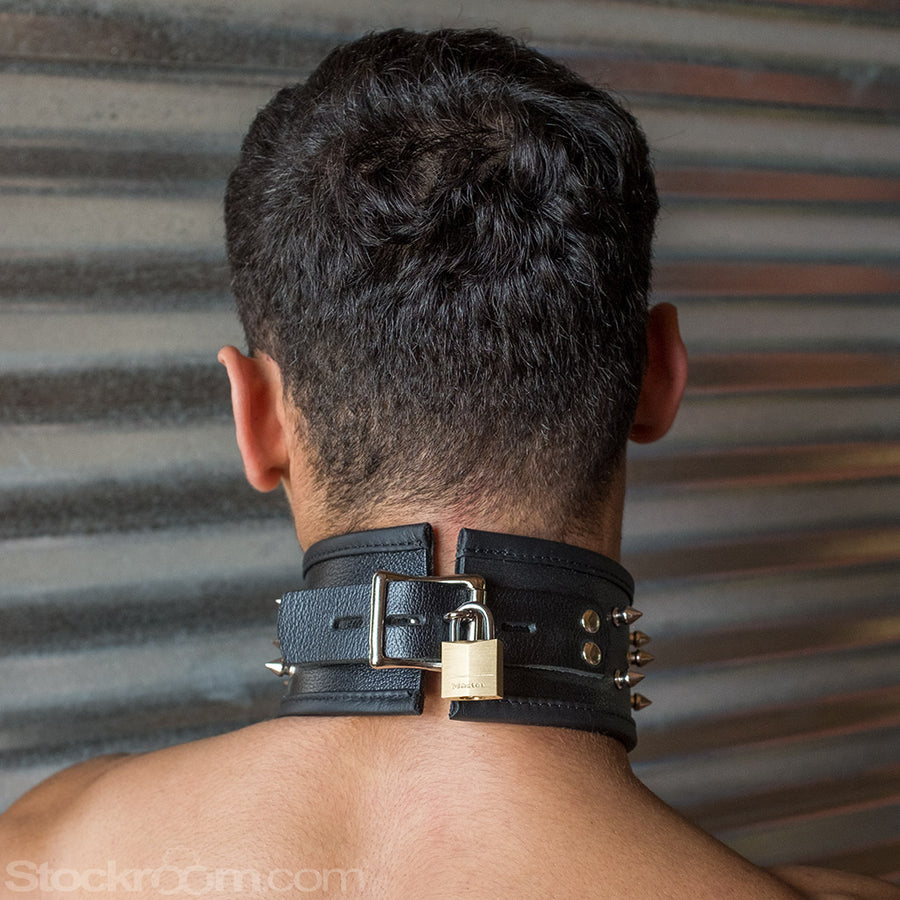 A close-up of the back of a man's head and neck is shown. He wears the BDSM Alpha Dog Leather Collar with Spikes. The buckle is padlocked shut with a brass padlock.