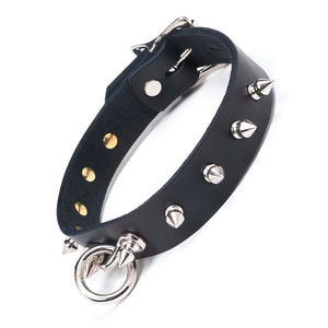 The Leather Collar with Spikes is shown against a blank background. It is made of black leather with metal hardware. There are spikes projecting outwards around the collar and a dangling O-ring in the front.