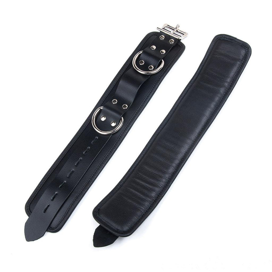 The Deluxe Padded Leather Ankle Restraints With D-Rings are shown uncuffed against a blank background, lying with the inside and outside visible. The inside is slightly raised because of the padding and the outside is shown with D-Rings.