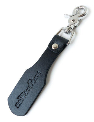 The Stockroom Branded Leather Keychain Paddle is shown against a blank background. They keychain is a small piece of black leather shaped like a paddle, attached to a metal snap hook, with The Stockroom logo branded onto it. 