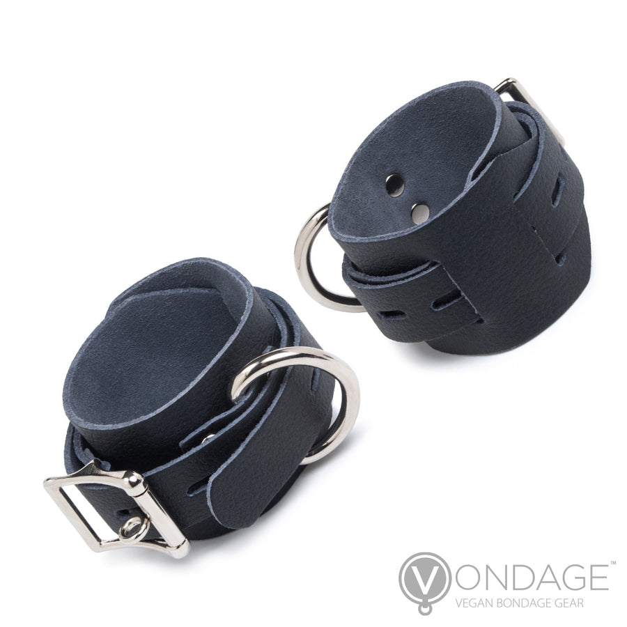 The Vondage Locking/Buckling Bondage Restraints, made of black faux leather and silver hardware, are shown against a blank background. The restraints are made of one wide piece of fabric, with a smaller notched piece wrapping around them to adjust their size.