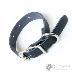 The Vondage Cock Ring is shown against a blank background. It is a thin, adjustable strip of black faux leather with a metal buckle closure.