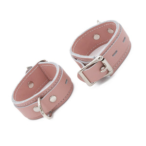 The Stupid Cute Wrist Cuffs are shown fastened against a blank background. The leather is pink with white edges and white stitching on the borders. They have a silver D-Ring and fasten with a lockable buckle.