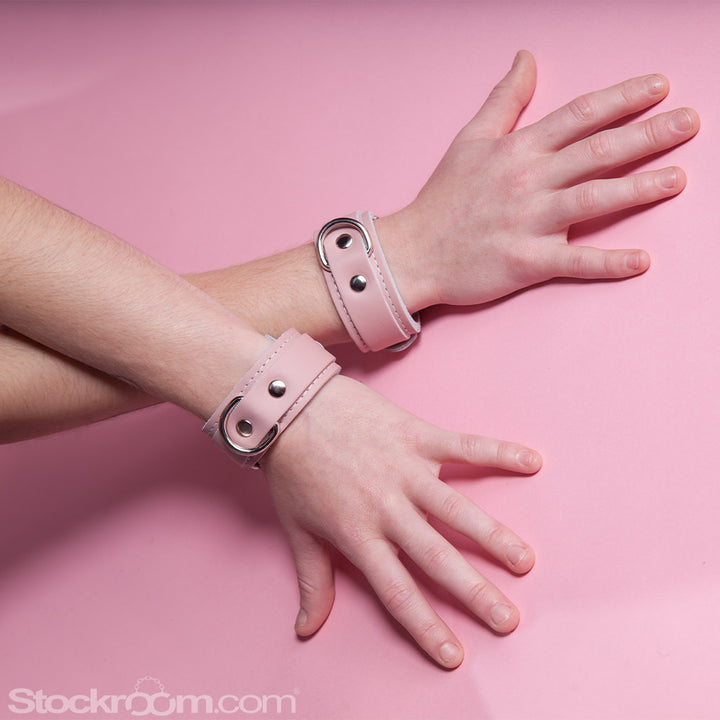 A close-up of a woman’s wrists with the Stupid Cute Wrist Cuffs on them is shown against a pink background.