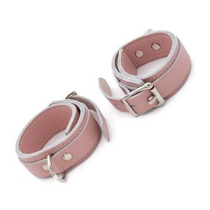 The Stupid Cute Ankle Cuffs are shown fastened against a blank background. The leather is pink with white edges and white stitching on the borders. They are adjustable and fasten with a lockable buckle.