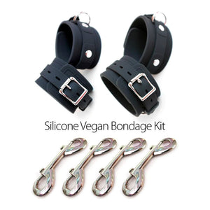 The contents of the Silicone Vegan Bondage Kit are shown against a blank background. The wrist and ankle cuffs, made of matte black silicone with silver hardware, have buckles and one D-ring each. Beneath the cuffs are four metal snap hooks.