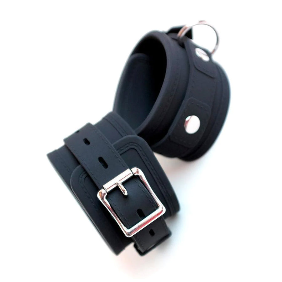 The wrist cuffs from the Silicone Vegan Bondage Kit are displayed against a blank background. They are made of matte black silicone with silver hardware. They are adjustable and have a buckle and one D-ring each.