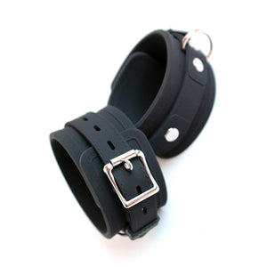 The ankle cuffs from the Silicone Vegan Bondage Kit are displayed against a blank background. They are made of matte black silicone with silver hardware. They are adjustable and have a buckle and one D-ring each.