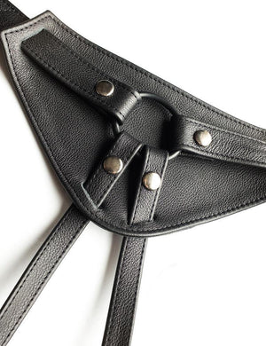 A close-up of the front piece of The Full Curves Leather Strap-on Harness in black is displayed against a blank background. 