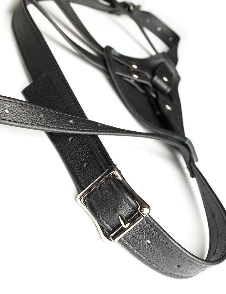 A close-up of the straps on The Full Curves Leather Strap-on Harness in black is displayed against a blank background. The straps are adjustable and are fastened with metal buckles.
