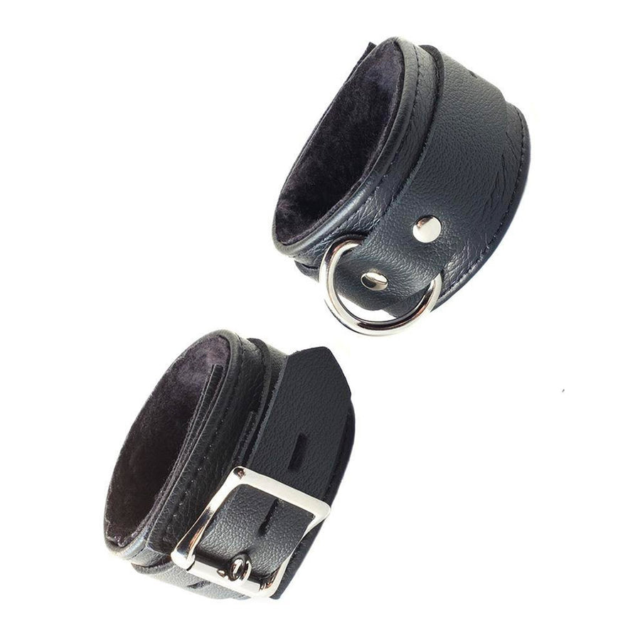A pair of black leather Fleece Lined Garment Leather Ankle Cuffs are shown cuffed against a blank background. The fuzzy, black fleece lining inside the cuffs is visible.