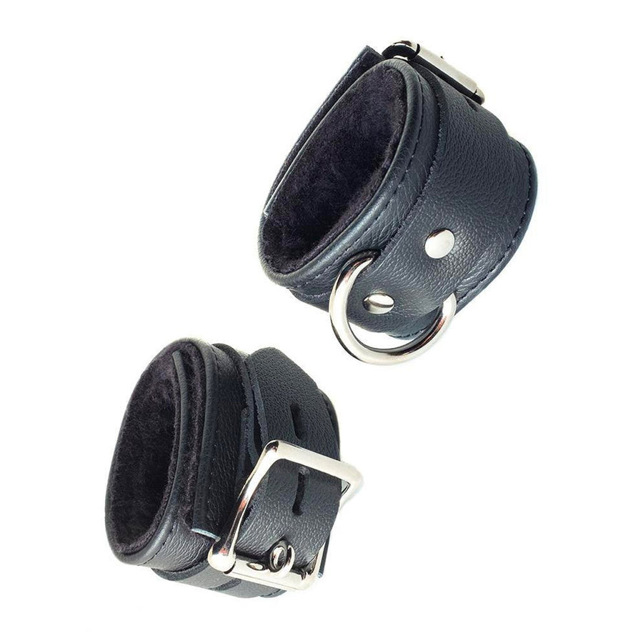 The Fleece Lined Garment Leather Wrist Cuffs are shown cuffed against a blank background. The cuffs are made of black leather and have silver hardware. The cuffs each have a D-ring and a buckle. The inside of the cuffs is lined with black fleece.