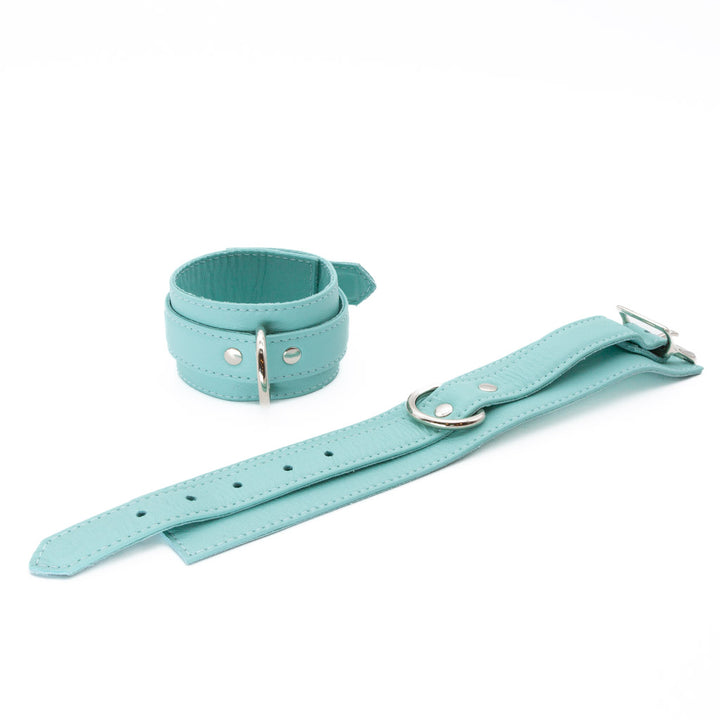 The Zoë Ligon x The Stockroom Limited Edition Mint Green Ankle Cuffs are displayed against a blank background, one buckled and one unbuckled. The restraints have an adjustable strap, metal D-rings, and a metal buckle.