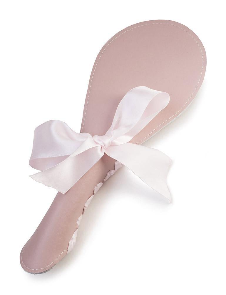 The Stupid Cute Pink Leather BDSM Spanking Paddle is shown against a blank background. It is shaped like a ping-pong paddle and has accent stitching around the border. It has a light pink ribbon laced up the back of the handle and tied in a bow.