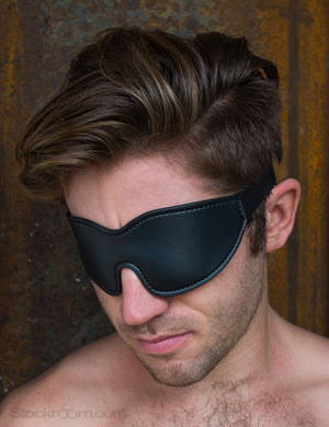 A close-up of a brunette man with facial stubble is shown wearing the Kinklab Padded Blindfold.