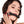 Load image into Gallery viewer, A woman with shoulder-length curly dark hair is shown against a blank background, wearing the Kinklab Silicone Bit Gag With A Leather Strap. Her nails are painted red, and her hands rest on her face below the gag. The gag is a rod made of black silicone.
