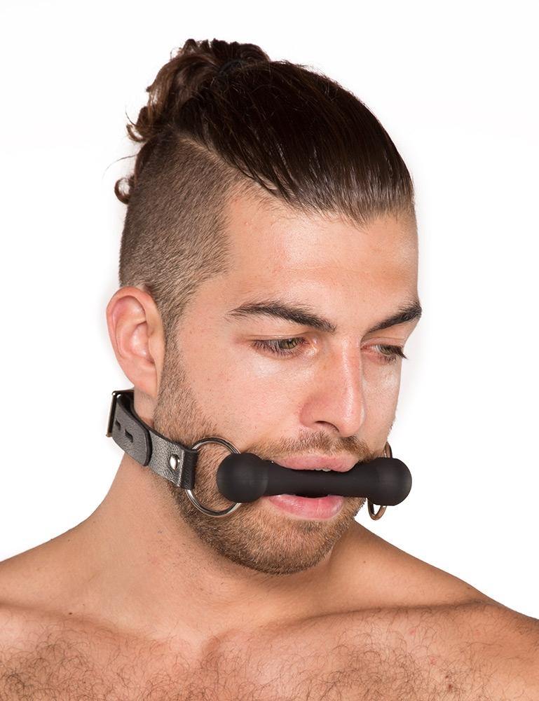  A man with dark brown hair that is shaved on the sides and pulled into a ponytail is shown wearing the Kinklab Silicone Bit Gag against a blank background.