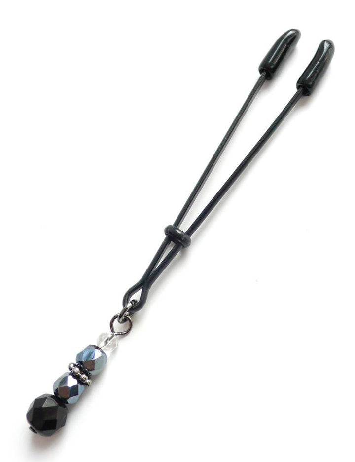 The Beaded Clit Clamp is displayed against a blank background. It is a black adjustable tweezer-style clamp with four decorative black and white beads dangling from the bottom.