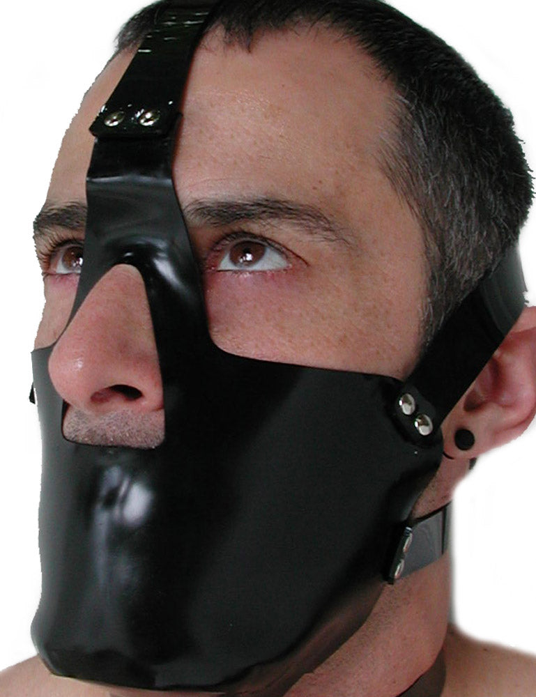 A close-up of a dark-haired man's face is shown against a blank background. He wears the rubber Head Harness with a Muzzle. It is a black muzzle that covers his mouth and chin and straps around his head.
