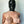 Load image into Gallery viewer, A topless woman is shown from the waist up, standing against a wall and covering her breasts with her hands. She wears the Extreme Rubber Hood zipped up, completely covering her face.
