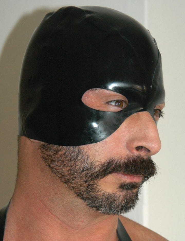 A close-up of a man with facial hair wearing the black Rubber Executioner's Hood is shown. The hood covers the top half of his head, surrounding his eyes and cutting off at the top of his nose.