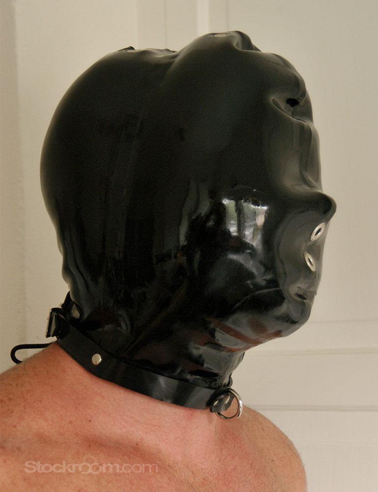 A man wearing the black Padded Rubber Hood is shown from the side. The hood completely encases his head and neck and has two small holes near the mouth and nose for air. There is a small metal D-ring at the neck.