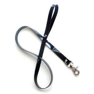 The BDSM 4' PVC Leash is shown against a blank background. It is made of a thin strip of shiny black PVC looped into a handle on one end and with a metal snap hook on the other.