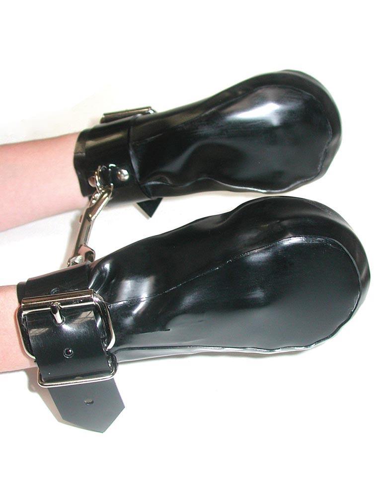 A person’s arms are held out in front of a white wall. Their hands are in the black Rubber Fist Mitts, which are black latex pouches with buckles around the wrists. The mitts each have a D-ring on the cuff, and they are hooked to each other with a snap hook.