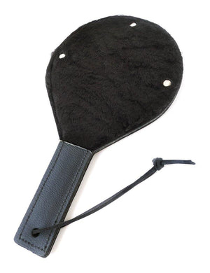 The Black Leather Gentle Persuasions Paddle is shown against a blank background with the fuzzy side facing up. The paddle is rounded with a straight leather handle with a wrist loop at the base. The paddle is covered in black faux fur.