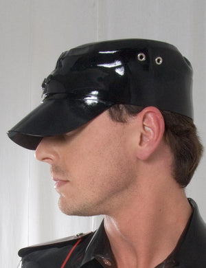 A headshot of a man in front of a white background. He wears the Rubber Soldier's Cap with Snaps by Syren Latex in black. The hat has a low brim and metal grommet accents on the sides.