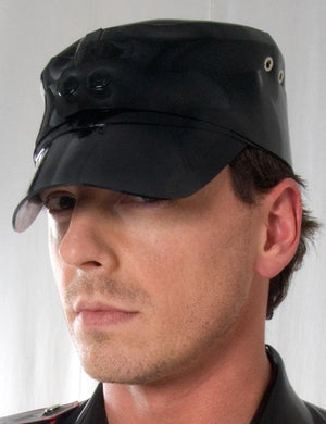 A headshot of a man in front of a white background. He wears the Rubber Soldier's Cap with Snaps by Syren Latex in black. The hat has a low brim and metal grommet accents on the sides.