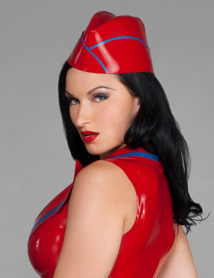 A woman with black hair and red lipstick wearing a red latex top poses in front of a grey background. She also wears the Latex Garrison Cap by Syren latex in red with blue trim.