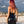 Load image into Gallery viewer, A woman with pink hair poses on a rooftop with a cloudy sky and the Los Angeles skyline behind her. She faces away from the camera and is wearing the Latex Halter Dress from Syren Latex in black.

