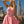 Load image into Gallery viewer, A blonde woman poses on a rooftop with the Los Angeles skyline in the background. She wears the Latex Swing Dress by Syren Latex in pink. The dress has tanktop sleeves and is form-fitting in the torso, and flares out at the waist.
