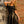 Load image into Gallery viewer, A blonde woman wearing the Ruffly Latex Rubber Heidi Dress in black by Syren Latex poses in front of a brick wall. The dress has a sweetheart neckline and is fitted through the torso with a flared skirt. Ruffle accents line the sleeves and neckline.
