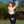 Load image into Gallery viewer, A topless woman with red hair poses outside on a grass lawn. Her arms are raised, with one arm covering her breasts. She wears the black latex Pencil Skirt from Syren Latex as well as black latex wrist-length gloves.
