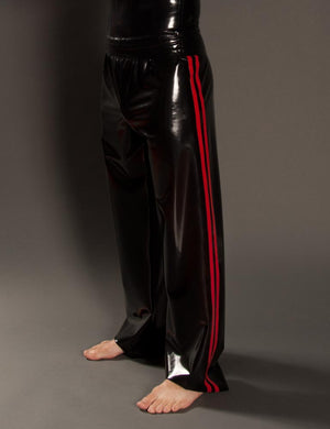 A close-up of a man's legs is shown in front of a grey backdrop. He wears the Men's Latex Track Pants by Syren Latex in black with red accents.