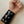 Load image into Gallery viewer, A close-up of a man&#39;s forearm is shown in front of a white wall. He wears the Latex Wrist Wallet by Syren Latex in black. The wallet resembles an armband and has two rows of three metal snaps.
