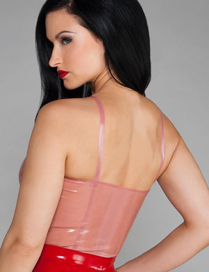 A woman with black hair and red lipstick wearing the Newmar Camisole by Syren Latex in transparent pink poses in front of a grey backdrop.