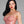 Load image into Gallery viewer, A woman with black hair and red lipstick wearing the Newmar Camisole by Syren Latex in transparent pink poses in front of a grey backdrop. The top has thin straps and a seamed bodice outlining the bust.
