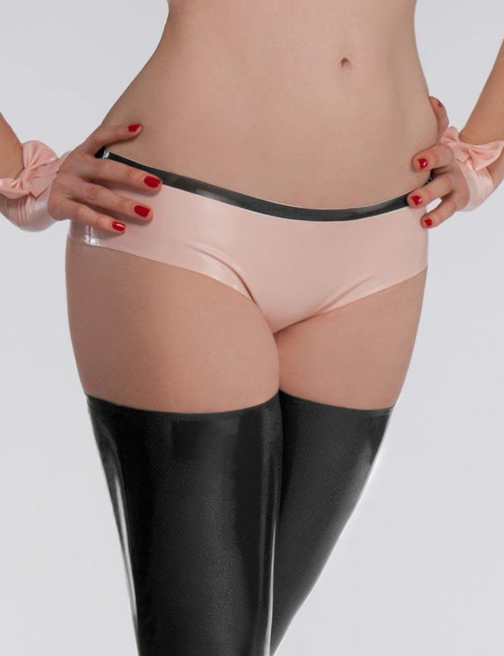A close-up of a woman's torso and thighs is shown against a grey back drop. She wears the Chloe Panty by Syren Latex, which is a lowrise boy short style, in baby pink with black trim. She also wears pink latex glovelettes and black latex stockings.