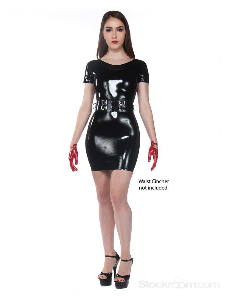 A brunette woman with red lipstick stands with a blank background. She wears The Jane Latex Dress by Syren Latex in black, as well as a black waist cincher, high heels, and red latex driving gloves. The hem of the dress ends at her mid-thigh.