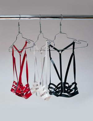 Three latex halter cage bras, one in red, one in white, and one in black, are shown hanging on clothes hangers from a metal rod. 